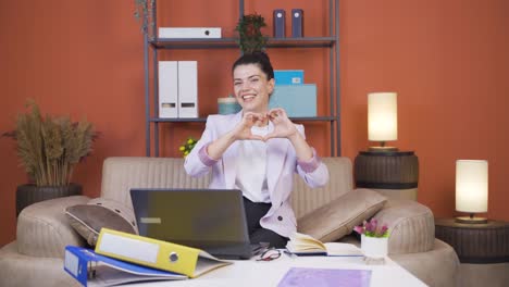 Home-office-worker-young-woman-makes-heart-symbol-looking-at-camera.